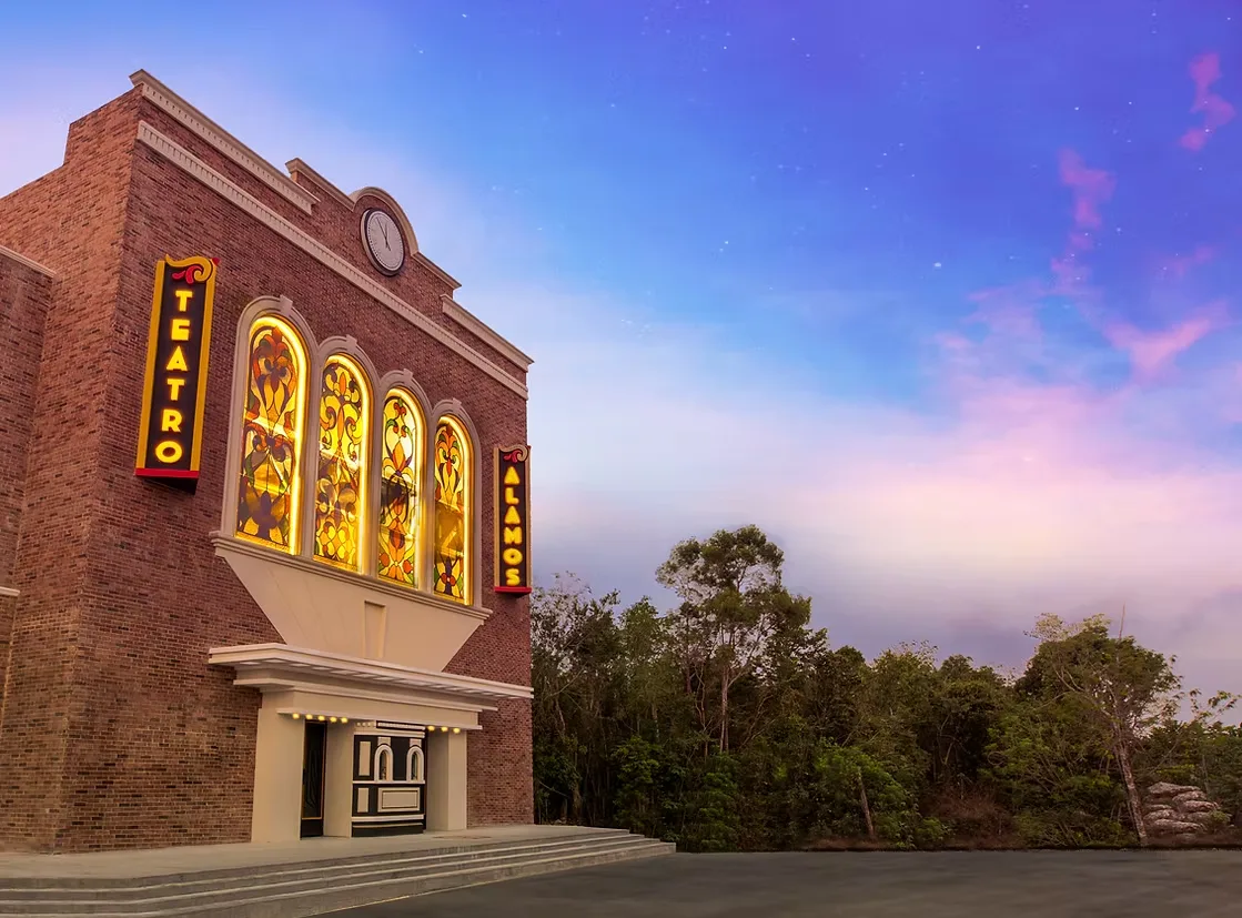 Fachada del Teatro Álamos al atardecer, con ventanales iluminados y letreros verticales